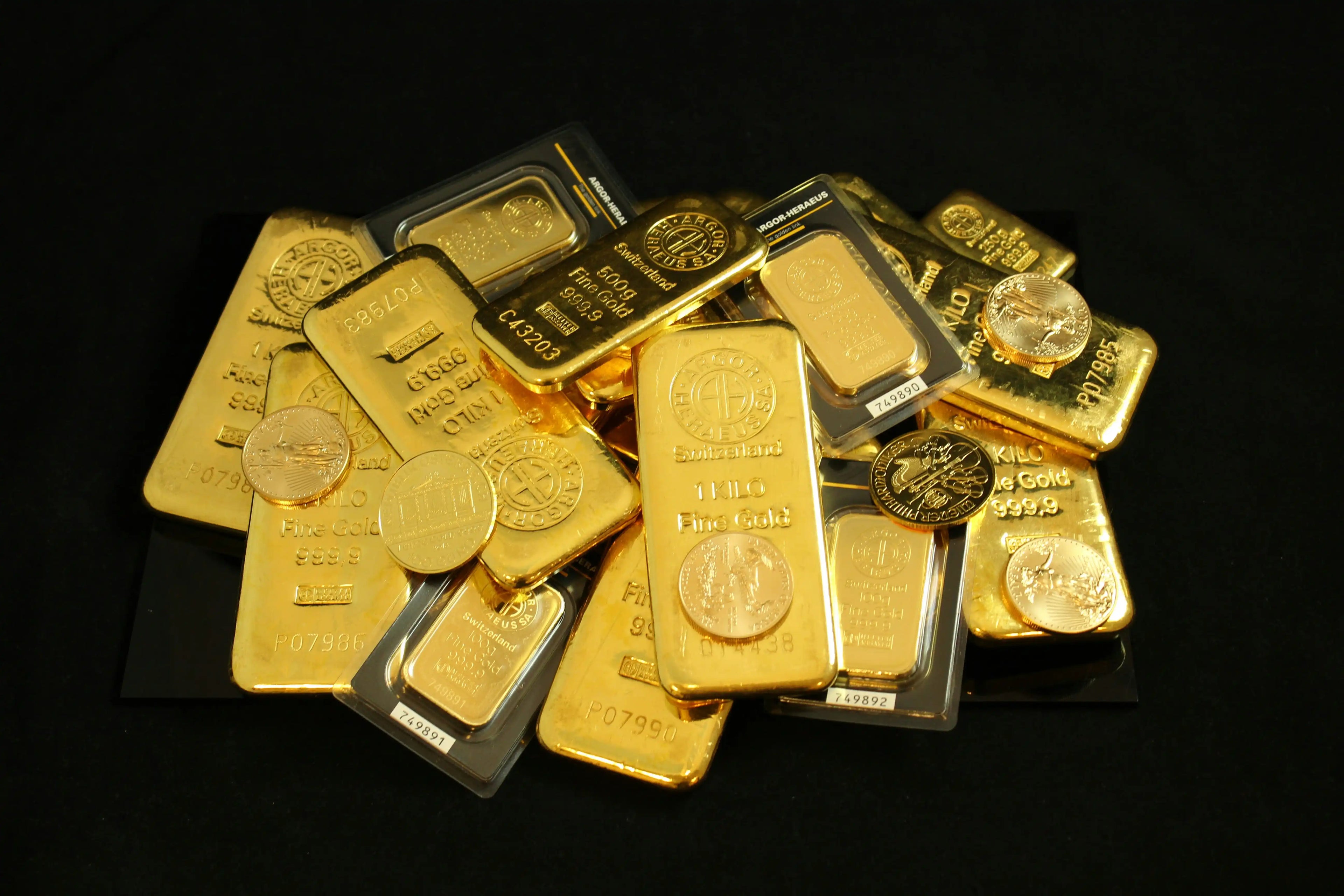 A pile of gold bullion bars and gold coins against a black background.